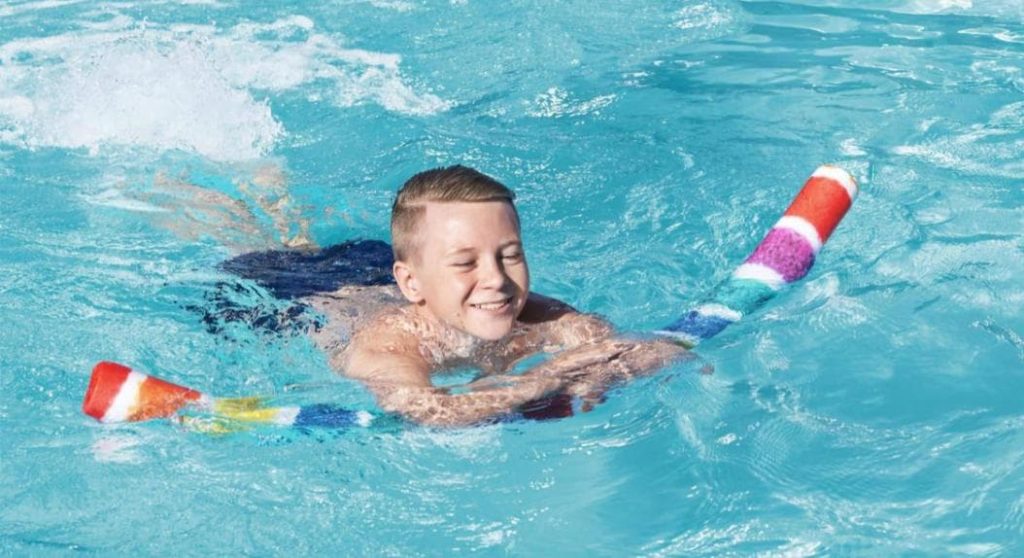 boy using a pool noodle as a float and kicking his legs